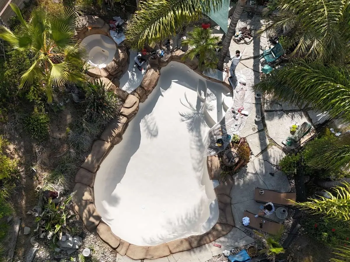 Aerial view of a pool remodel in progress with fresh white plaster and crew working around the shell