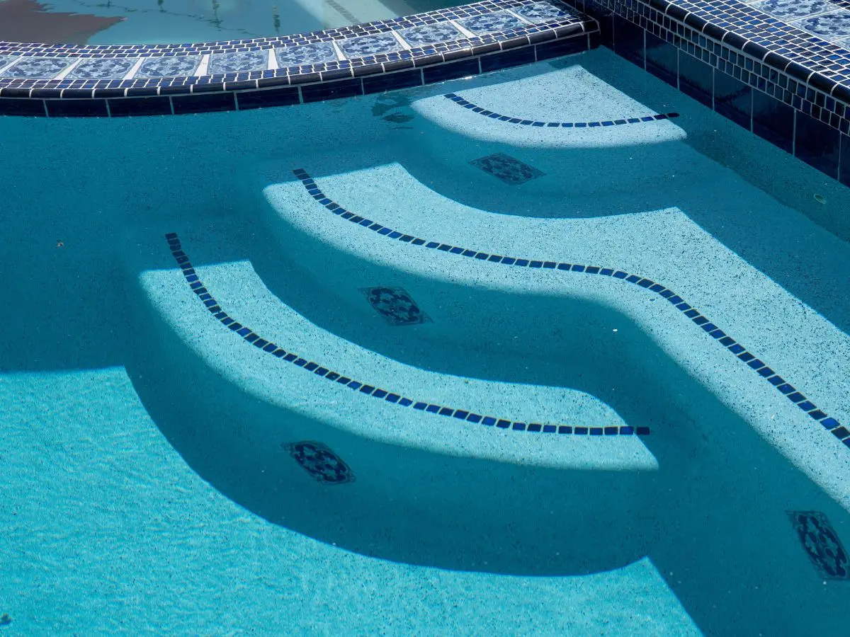 Pool steps with blue mosaic tile inlays and decorative blue and white waterline tile