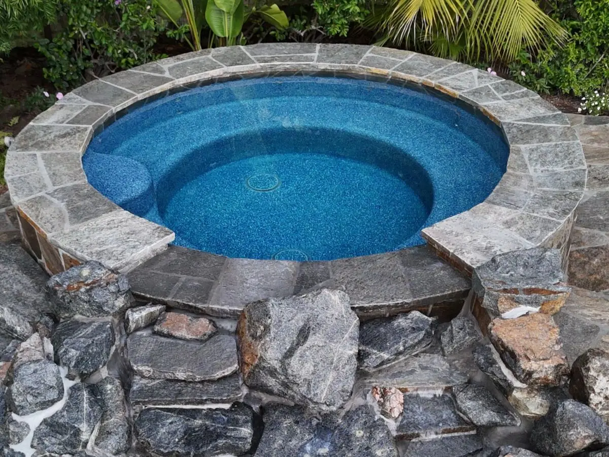 Round raised spa finished in blue pebble with flagstone coping and natural stone facing
